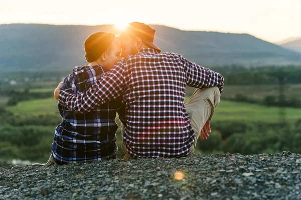 Een jong echtpaar in de liefde zit leunend tegen elkaar op de top van de berg bij zonsondergang. Zachte paar op romantische zonsondergang achtergrond. — Stockfoto