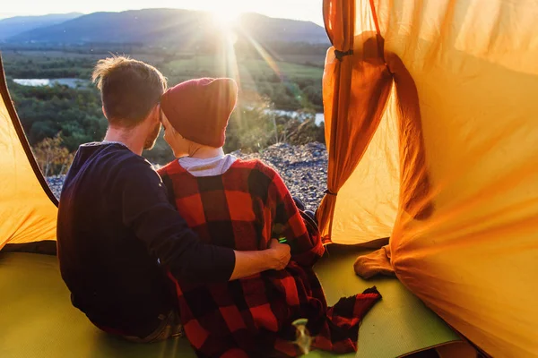 Blick aus dem Zelt eines jungen kaukasischen verliebten Paares, während sie bei Sonnenuntergang auf dem Hintergrund der Berge sitzen. Blick nach hinten. — Stockfoto