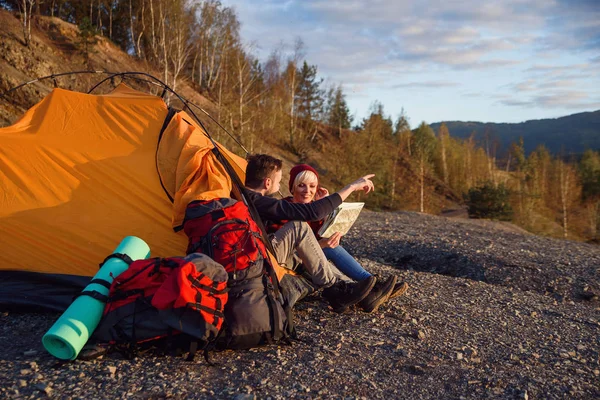 Jovem homem e namorada explorando mapa na montanha durante o dia ensolarado enquanto eles estão sentados na tenda . — Fotografia de Stock
