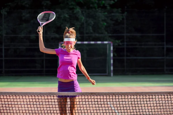 快乐的女子网球选手跳到网边大笑，庆祝她在网球比赛中获胜。体育、保健理念. — 图库照片