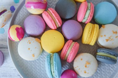 Mavi plaka ve beyaz ahşap arka plan üzerinde çok renkli Fransız makarna kek kapatın. Taze çilek ile beyaz, sarı, pembe, mor ve gri fransız makarna.
