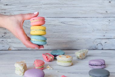 Beyaz ahşap arka plan üzerinde renkli macarons ile kadın elini kapatın.