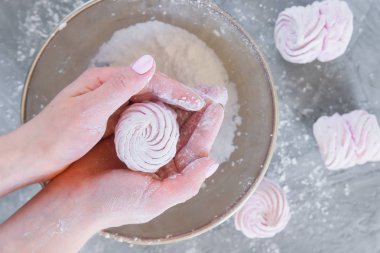 Yakın kadın elleri şeker pudraile plaka bir arka plan karşı taze hazırlanmış ev yapımı marshmallow tutar.