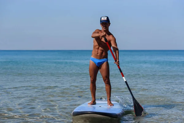 Sporty healthy person stands on his surfboard on the water, and rowing by oar. The concept of sporty and healthy lifestyle.