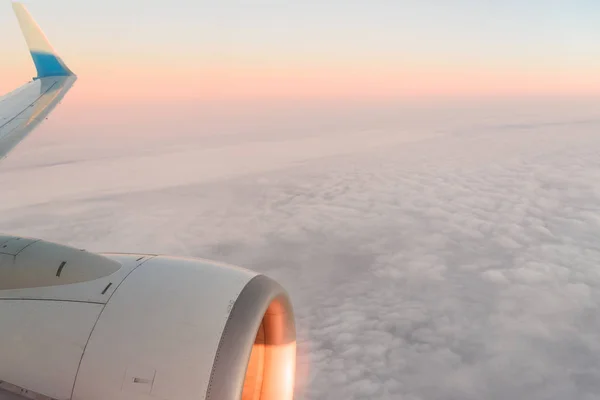 The view from the airplanes illuminator to the wing, airplane turbine and fluffy clouds at sunrise. Flying over the clouds — Stock Photo, Image