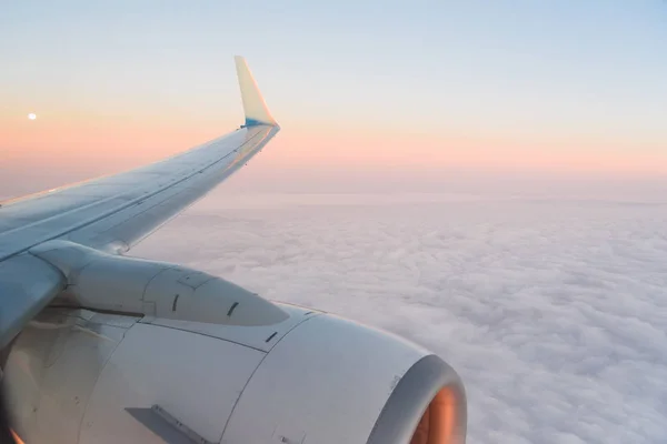 The view from the airplanes illuminator to the wing, airplane turbine and fluffy clouds at sunrise. Flying over the clouds
