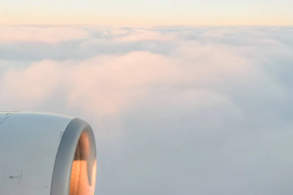 Вид від ілюмінатора літаків до крила, турбіни літака і пухнасті хмари на сході сонця. Політ над хмарами — стокове фото