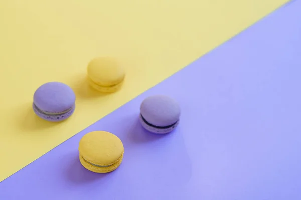 Sweet tasty violet and yellow french macaron cakes on yellow and violet background.