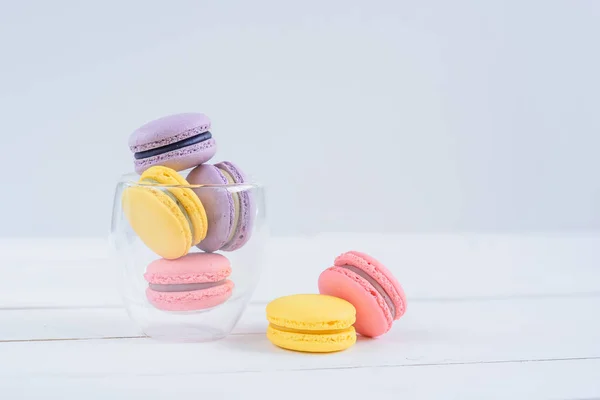 Delicious colorful macarons in a transparent glass cup on white wooden background. — Stock Photo, Image