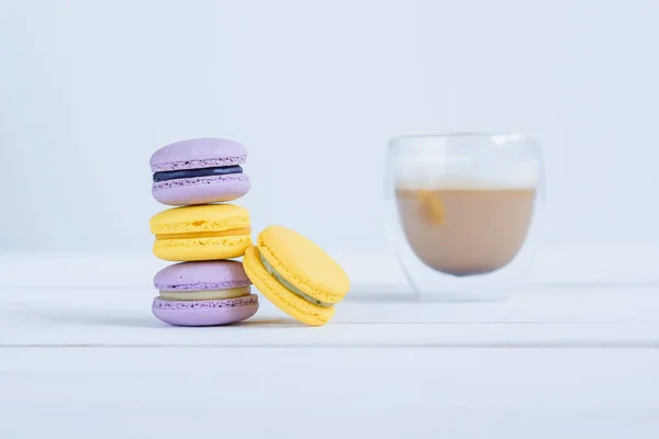 Leckere violette und gelbe Macarons und Tasse Latte auf weißem Holzhintergrund. — Stockfoto