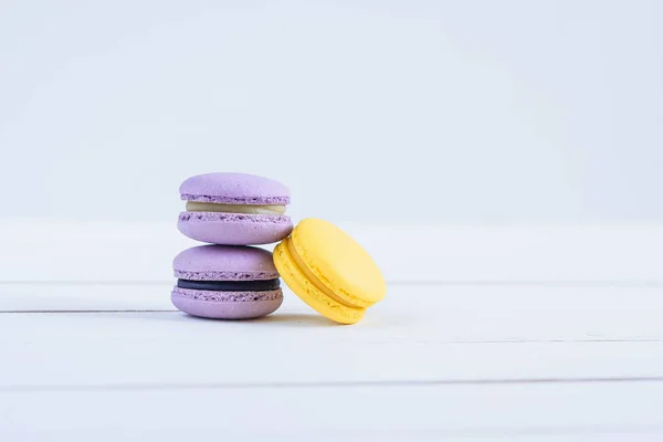 Köstliche violette und gelbe Macarons auf weißem Holzhintergrund. — Stockfoto