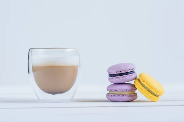 Вкусные фиолетовые и желтые макароны и чашка латте на белом деревянном фоне . — стоковое фото