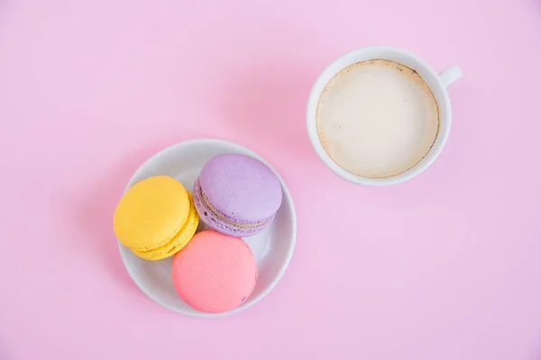 Tasty sweet macarons on the plate and cup of fragrant morning coffee. French macaroons on pink background. — Stock Photo, Image