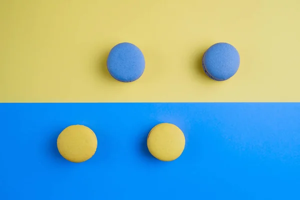 Sweet tasty blue and yellow french macaron cakes on yellow and blue background.