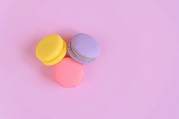 Tasty violet, pink and yellow french macaron cakes on pink background.