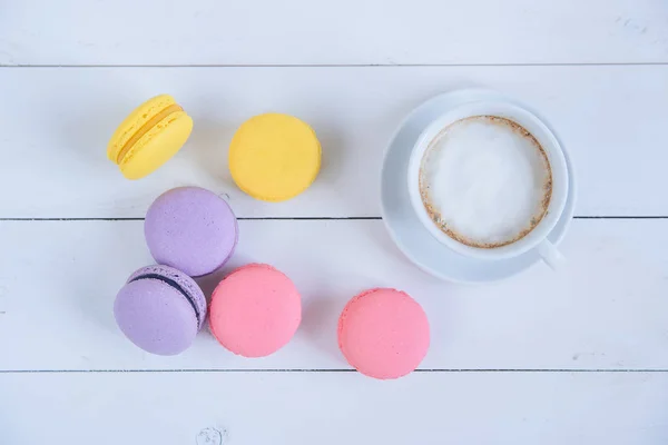 Sweet delicious colorful macarons and cup of coffee on white wooden background. — Stock Photo, Image