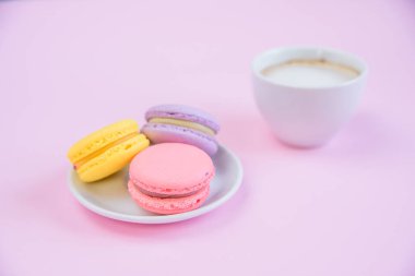 Tabakta lezzetli tatlı makarnalar ve bir fincan kokulu sabah kahvesi. Pembe arka plan üzerinde Fransız makaronlar.