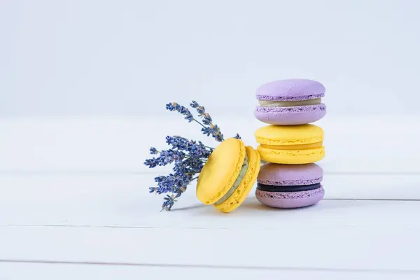 Вкусные фиолетовые и желтые макароны и ветвь ароматной лаванды на белом деревянном фоне . — стоковое фото