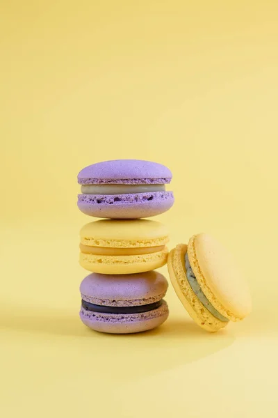 Tasty violet and yellow french macaron cakes on yellow background.