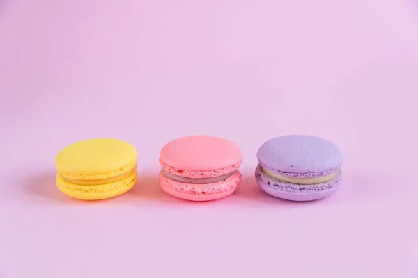 Tasty violet, pink and yellow french macaron cakes on pink background.