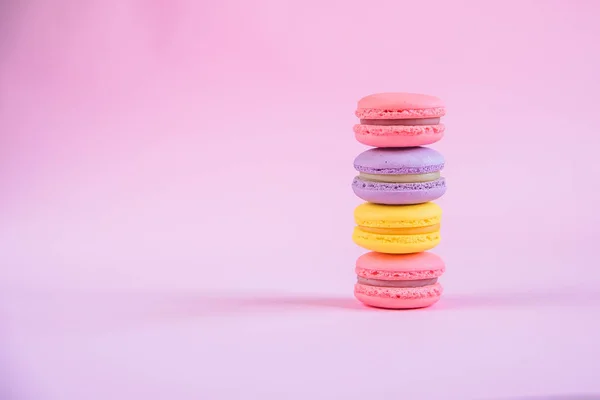 Tasty violet, pink and yellow french macaron cakes on pink background.