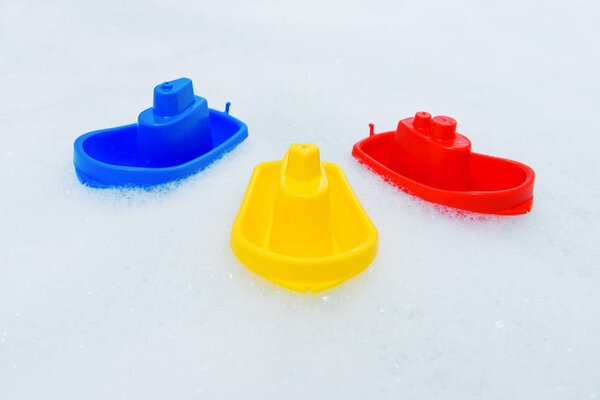 Plastic multicolored toy boats on foam bath.