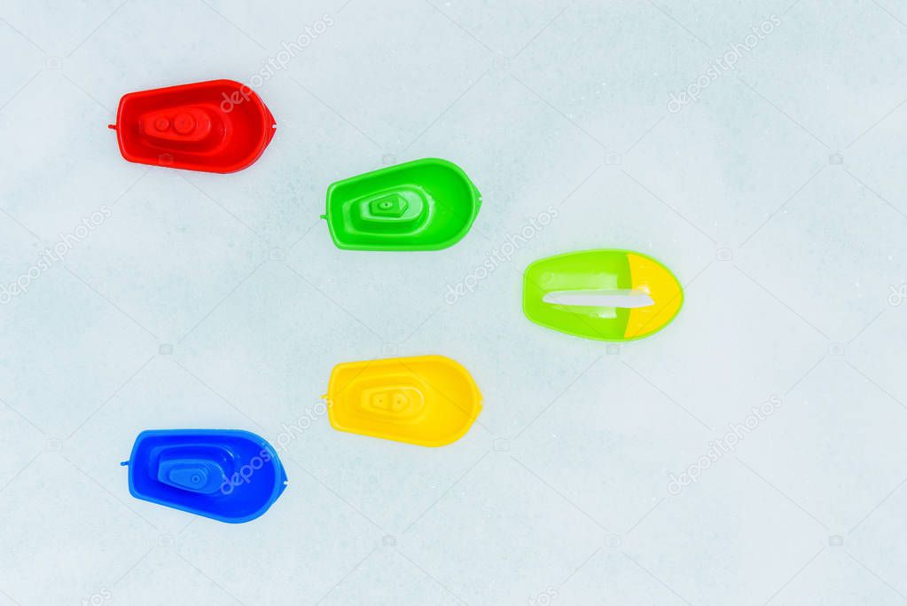 Plastic multicolored toy boats on foam bath.