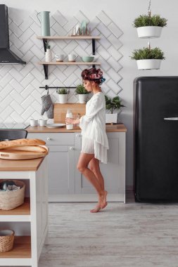 Elinde bir şişe süt tutan sevimli güzel bir kadın. Güzel kız modern rahat mutfakta kahvaltı hazırlanıyor.