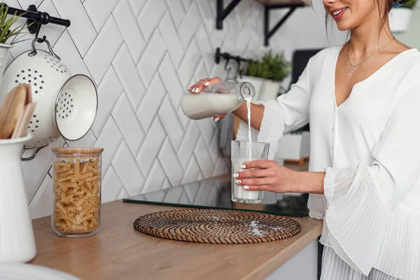 Güzel kız şık rahat mutfakta, bir cam içine bir carafe süt döker. Sağlıklı beslenme ve diyet konsepti.