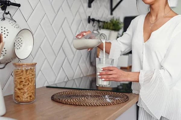 Güzel kız şık rahat mutfakta, bir cam içine bir carafe süt döker. Sağlıklı beslenme ve diyet konsepti.