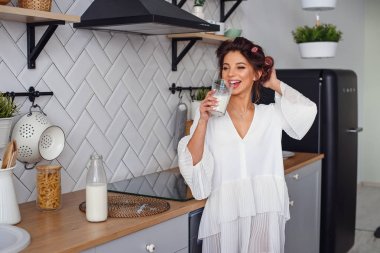 Büyüleyici güzel kadın şık mutfakta sabah taze süt içecekler. Güzel kız modern rahat mutfakta kahvaltı hazırlanıyor.