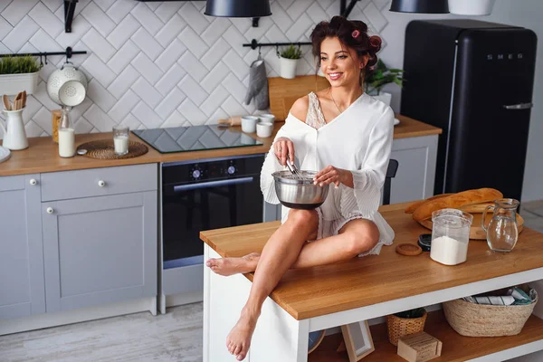Beyaz bornoz çekici kız şık modern mutfakta bir metal plaka bir hamur yoğurur. Genç güzel kadın ev mutfağında pişirme.