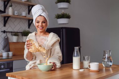 Kafasına bornoz ve havlu içinde büyüleyici kadın gevreği ve süt ile sağlıklı bir kahvaltı hazırlar. Kız sabah şık rahat mutfakta bir kahvaltı var.