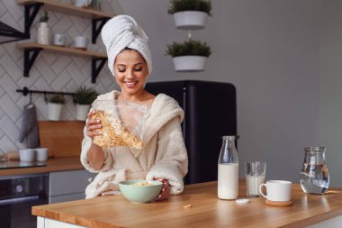 Kafasına bornoz ve havlu içinde büyüleyici kadın gevreği ve süt ile sağlıklı bir kahvaltı hazırlar. Kız sabah şık rahat mutfakta bir kahvaltı var.