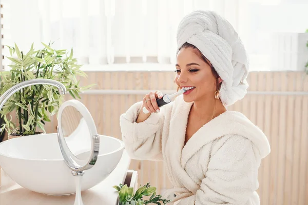 Молода щаслива дівчина чистить зуби вранці перед дзеркалом . — стокове фото