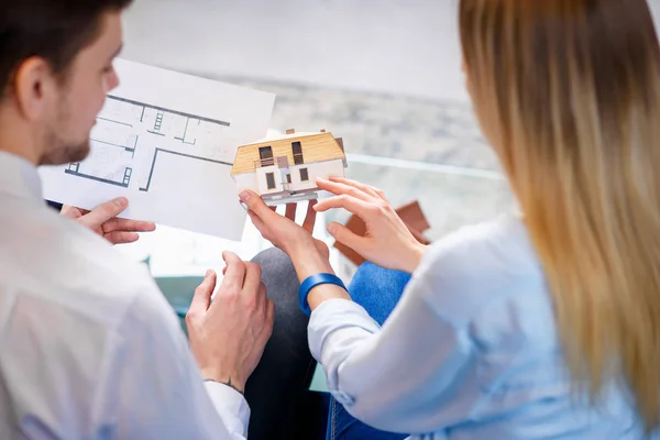 Caucasian man and woman discussing design of 3d model and sketch of future house.