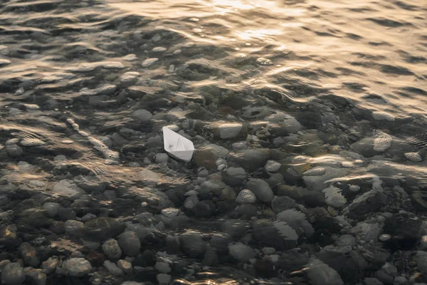 White paper boat floats on water with waves and ripples.