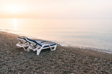 Güneşin doğuşunda deniz plajında iki plastik şezlong. Yaz tatili konsepti.