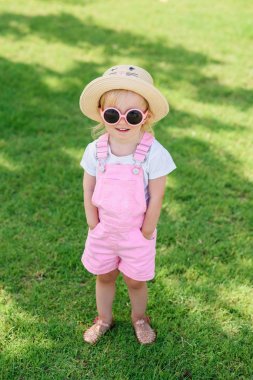 Pembe Tulum, şapka ve pembe gözlük şık kız yeşil çim üzerinde yürür. Yaz tatili konsepti.