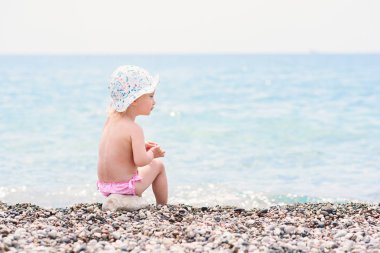 Sevimli Toddler kız sıcak yaz gününde deniz plajında oturur ve taşlar ile oynuyor.