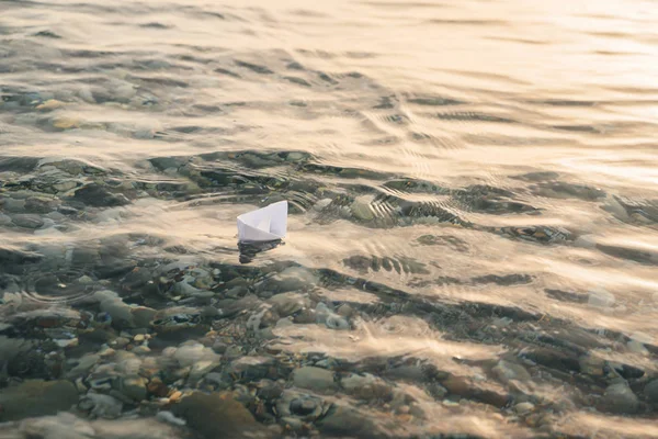Paper boat floats on water with waves and ripples. Lonely toy boat at the sea.