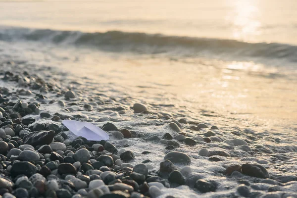 Barco de papel encontra-se à beira-mar ao nascer do sol . — Fotografia de Stock