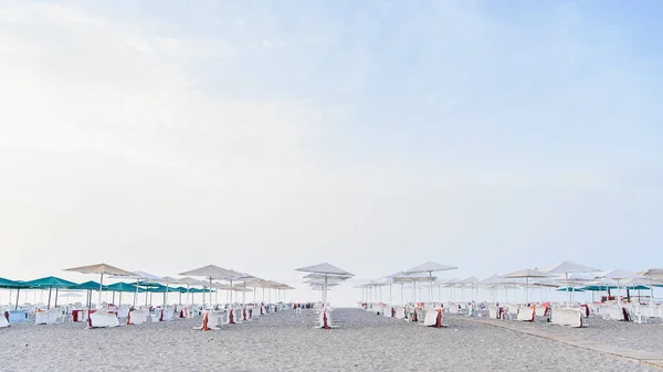 Un montón de tumbonas blancas bajo un paraguas en una playa limpia por la mañana . — Foto de Stock