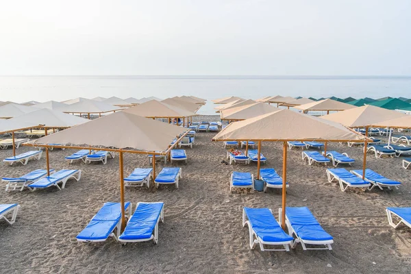 Muchas tumbonas de plástico y sombrillas en la playa al amanecer. Concepto vacaciones de verano . — Foto de Stock
