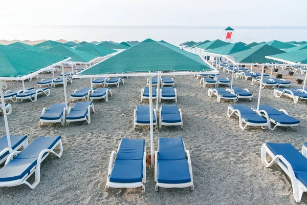 Muchas tumbonas de plástico y sombrillas en la playa al amanecer. Concepto vacaciones de verano . — Foto de Stock