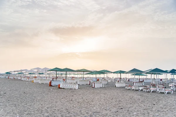 Un montón de tumbonas blancas bajo un paraguas en una playa limpia al atardecer o al amanecer . — Foto de Stock