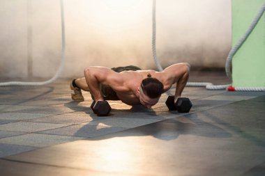 Spor salonunda eğitim sırasında dumbbells ile şınav yapıyor Genç güçlü adam.