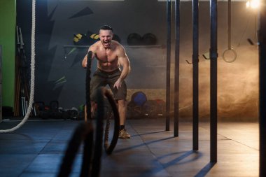 Yakışıklı güçlü adam fitness salonunda savaş halatları ile kaslar için egzersizyapıyor.