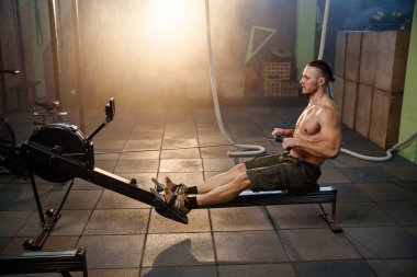 Spor salonunda simülatörleri üzerinde egzersiz yapan güçlü genç adam.