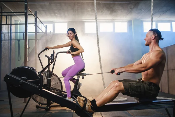 Joven pareja deportiva haciendo ejercicios en los simuladores en el gimnasio . — Foto de Stock